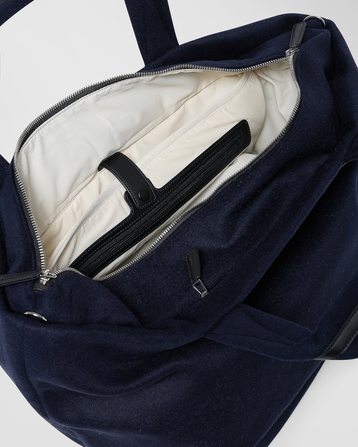 A close-up product photo of an open Essence Wool Tote bag, showcasing its cream-coloured interior lining, black straps, and silver zipper hardware.