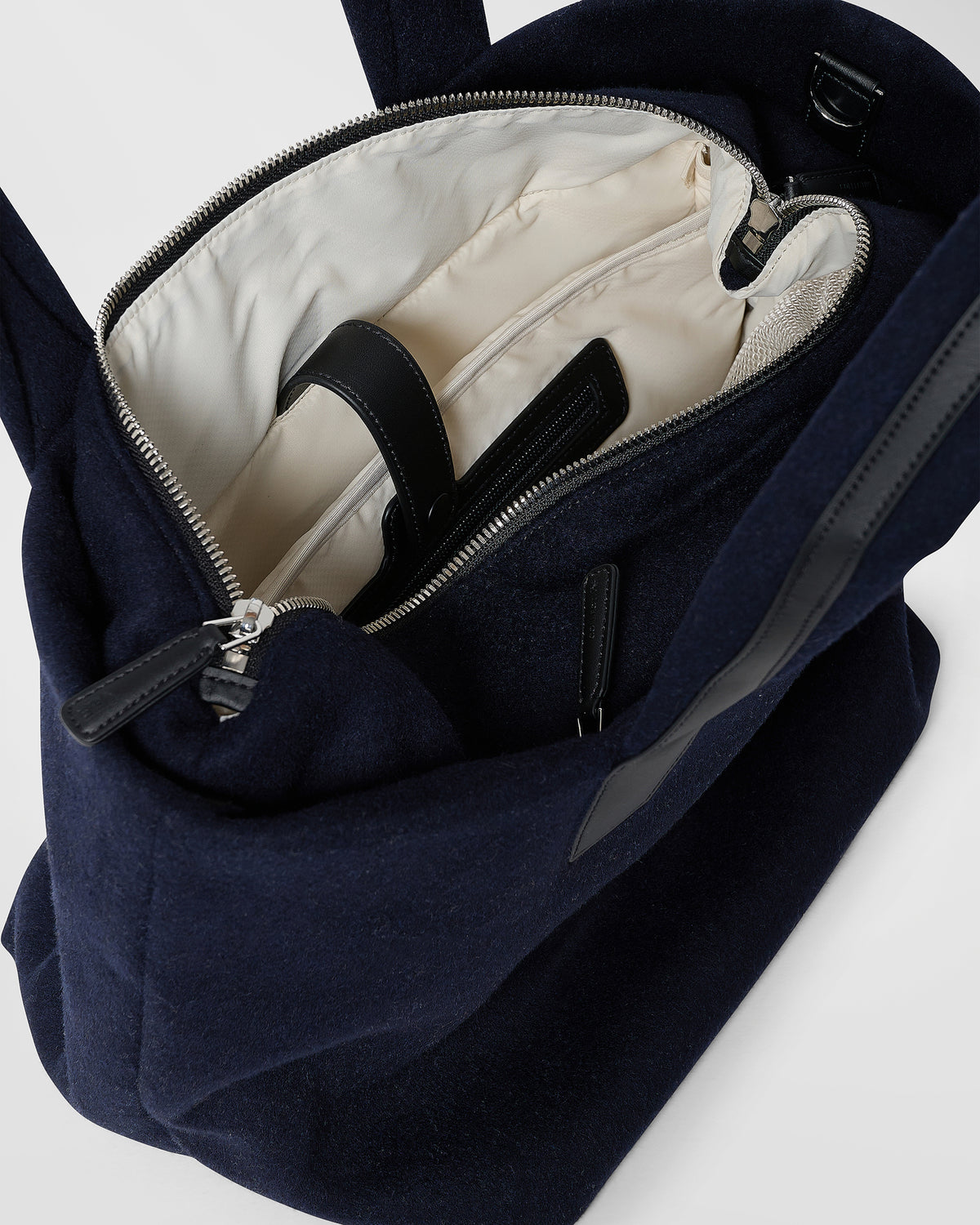 A close-up product photo of an open Essence Wool Tote bag navy, showcasing its cream-colored interior lining, black straps, and silver zipper hardware.