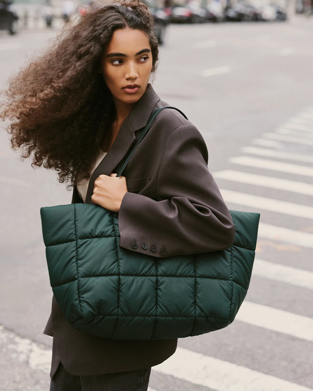 Woman walking on a crosswalk carrying the Porter Marché handbag in Bottle Green by VEE COLLECTIVE.
