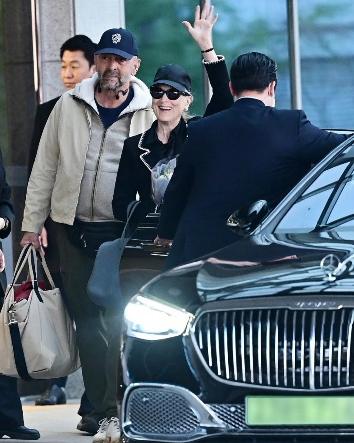 A picture featuring people boarding a black luxury car with a visible brand logo, carrying a beige Essence Trench Weekender bag.