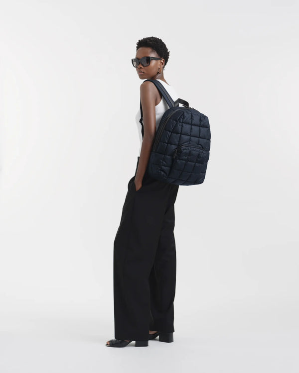 On-body picture of a woman carrying the Porter Backpack in Dark Navy by Vee Collective, wearing a minimalistic outfit against a clean studio background.