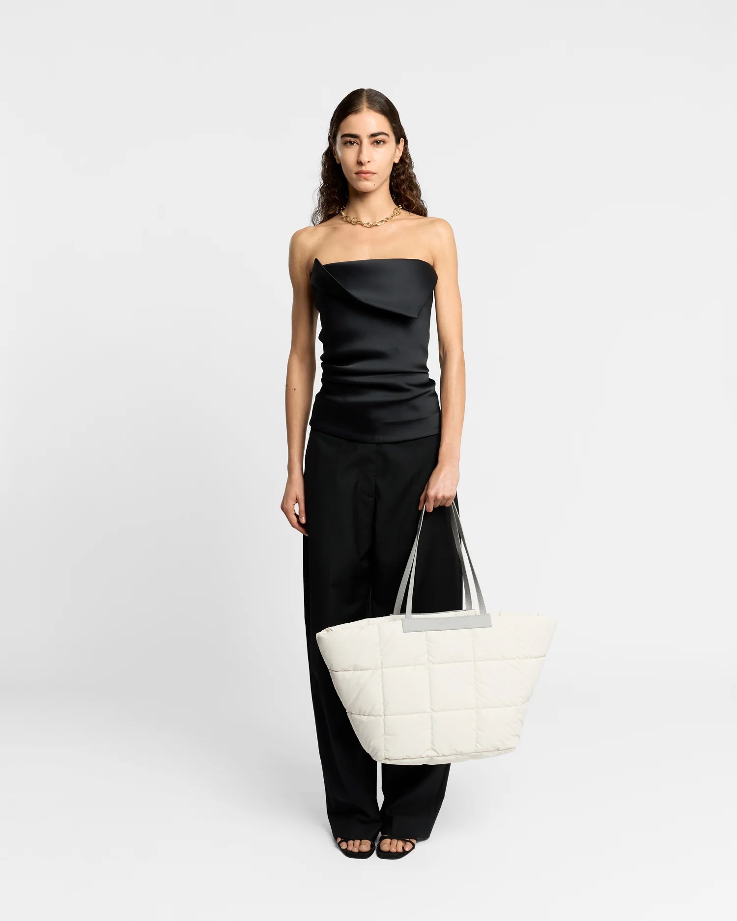 On-body picture of a woman holding the Porter Basque Tote Bag in Barely Beige by Vee Collective, wearing a minimalistic outfit against a clean studio background.
