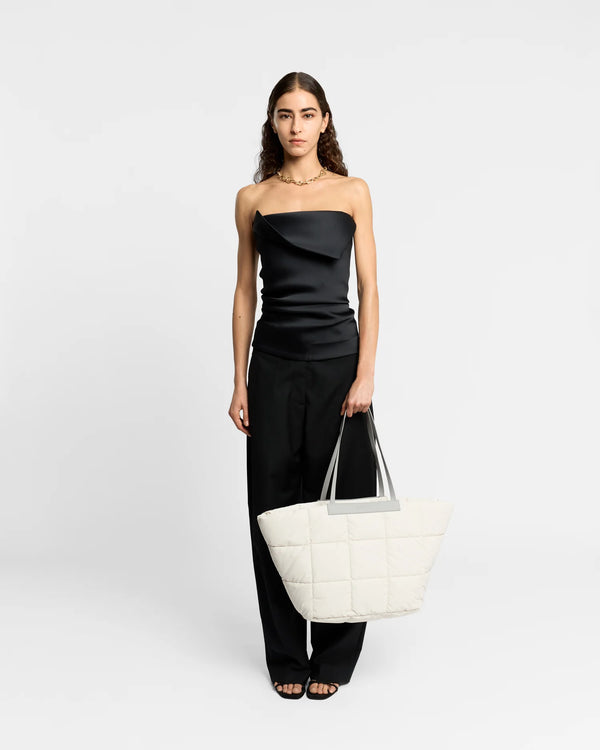 On-body picture of a woman holding the Porter Basque Tote Bag in Barely Beige by Vee Collective, wearing a minimalistic outfit against a clean studio background.
