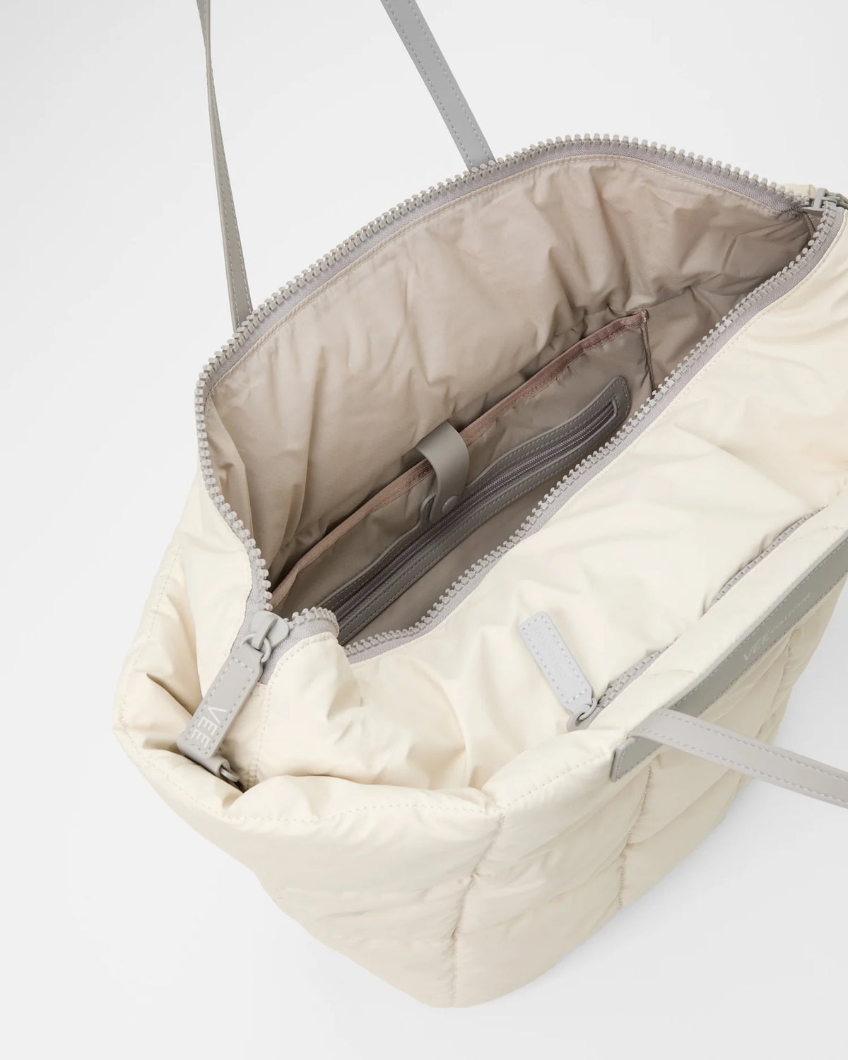 Open Vee Collective Porter Basque Tote Bag in Barely Beige, showing the quilted exterior, top zipper, and interior compartments of the tote bag.