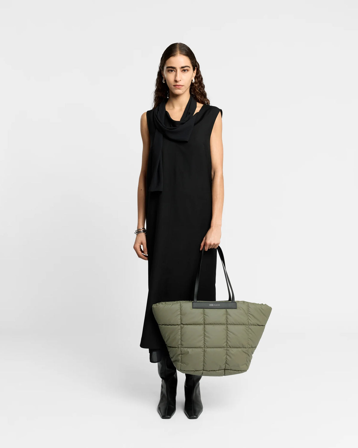 Woman wearing a clean outfit holding the Vee Collective Porter Basque Tote Bag in Moss, shown in profile against a clean background.