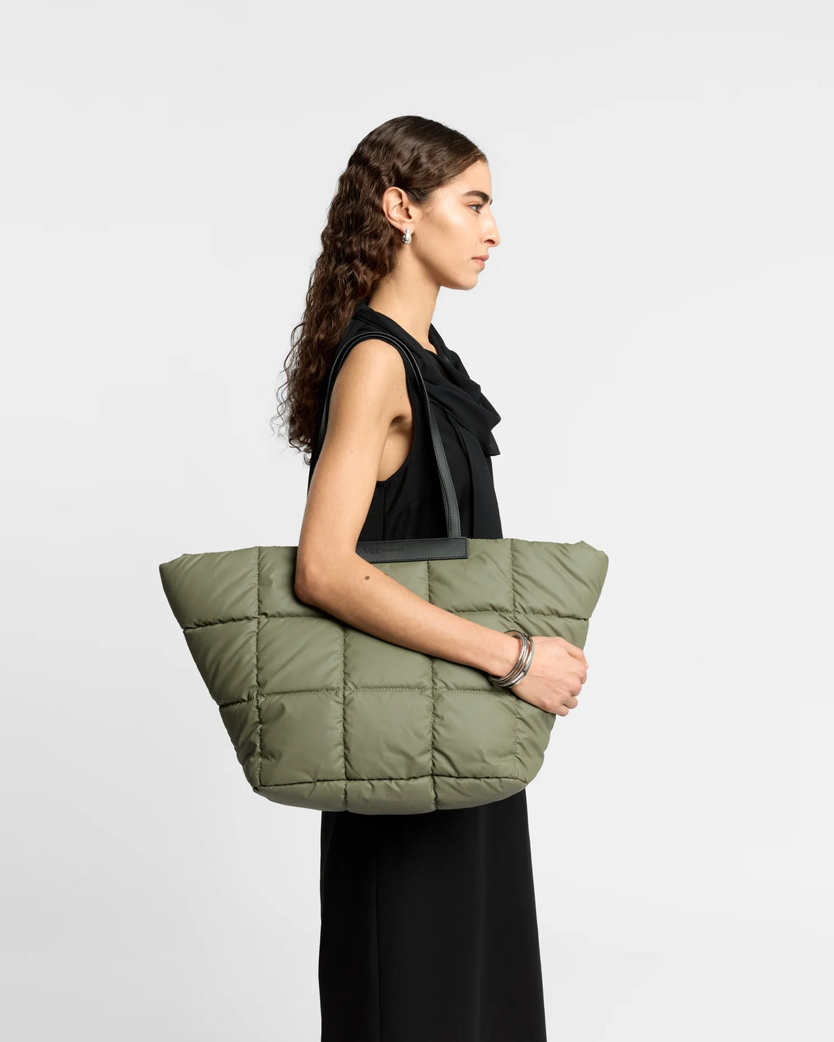 Woman wearing a clean outfit holding the Vee Collective Porter Basque Tote Bag in Moss, shown against a clean background.