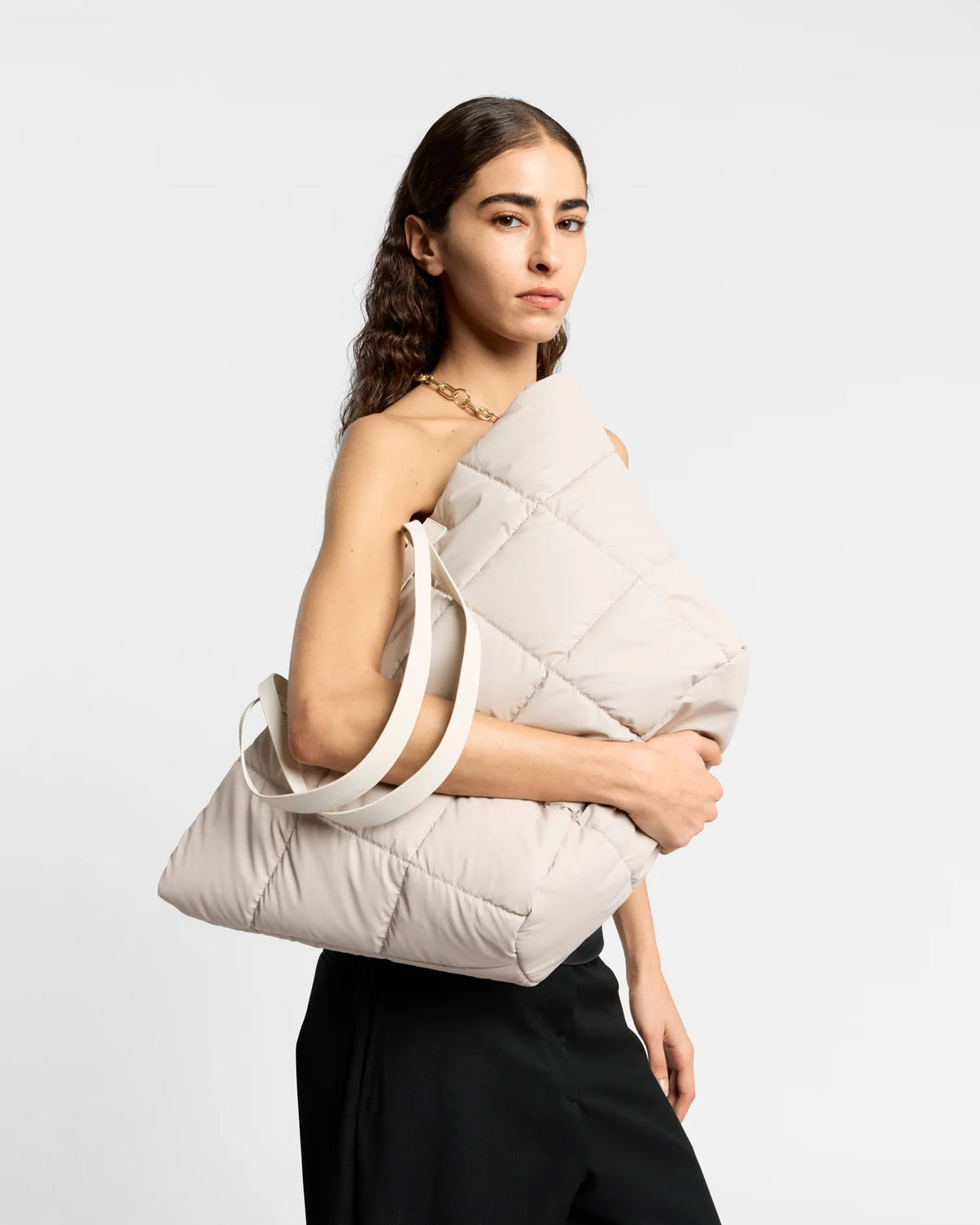 On-body picture of a woman holding the Porter Basque Tote Bag in Soft Taupe by Vee Collective under her arm, wearing a minimalistic outfit against a clean studio background.