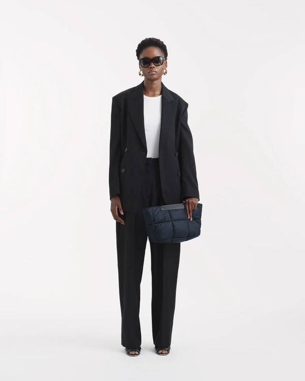 On-body picture of a woman holding the Porter Basque Clutch Bag in Dark Navy by Vee Collective, wearing a minimalistic outfit against a clean studio background.