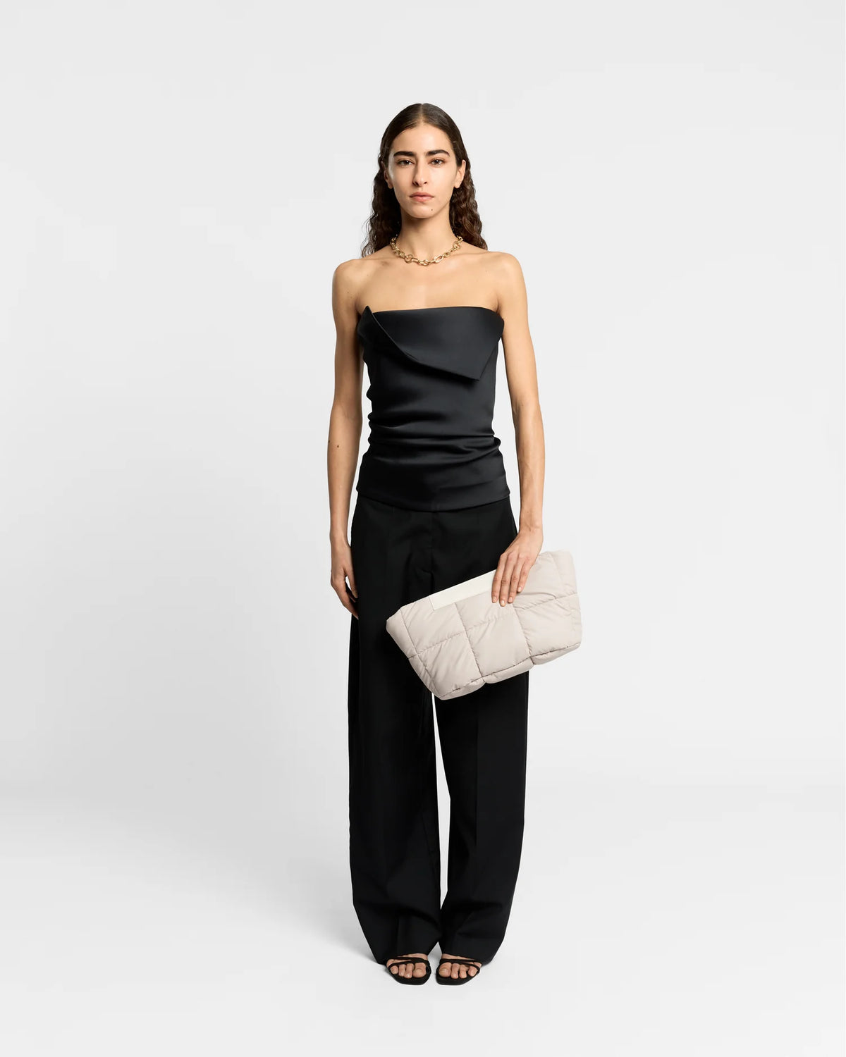 On-body picture of a woman holding the Porter Basque Clutch Bag in Soft Taupe by Vee Collective, wearing a minimalistic outfit against a clean studio background.
