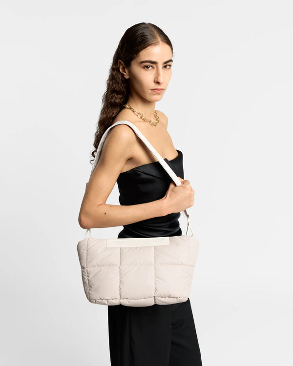 On-body picture of a woman carrying the Porter Basque Clutch Bag in Soft Taupe by Vee Collective over her shoulder with the attachable crossbody strap, wearing a minimalistic outfit against a clean studio background.