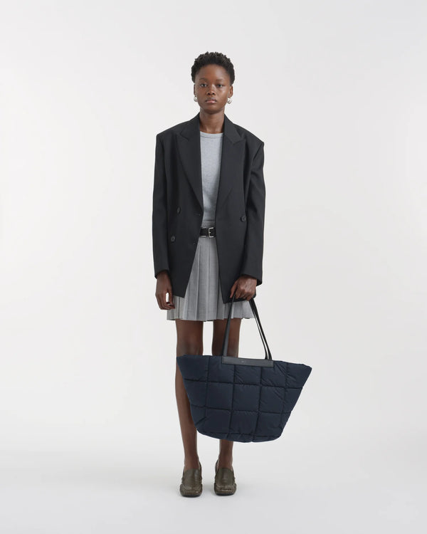 On-body picture of a woman holding the Porter Basque Tote Bag in Dark Navy by Vee Collective, wearing a minimalistic outfit against a clean studio background.