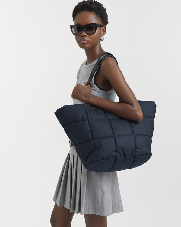 On-body picture of a woman carrying the Porter Basque Tote Bag in Dark Navy by Vee Collective, wearing a minimalistic outfit against a clean studio background.
