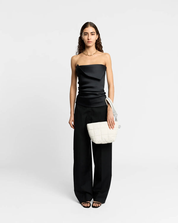 On-body picture of a woman carrying the Porter Clutch Bag in Barely Beige by Vee Collective, wearing a minimalistic outfit against a clean studio background, with the attachable wristlet worn on her wrist.