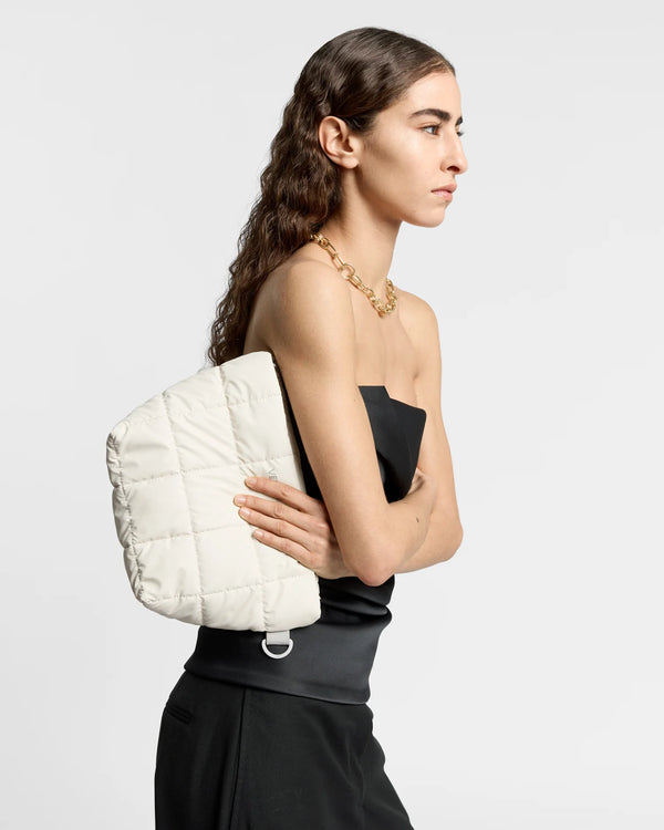 On-body picture of a woman holding the Porter Clutch Bag in Barely Beige by Vee Collective, wearing a minimalistic outfit against a clean studio background.