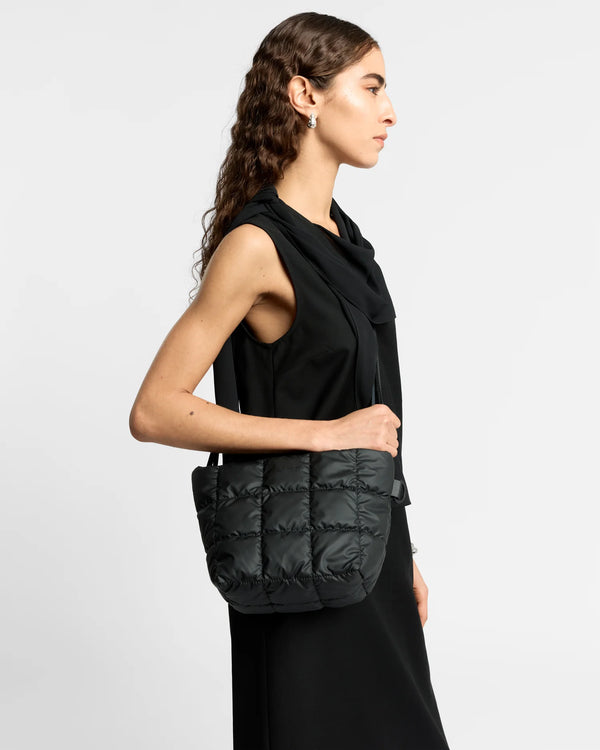 Woman in a minimal, clean outfit holding the Vee Collective Porter Clutch Bag in black, shown with its attachable crossbody strap.