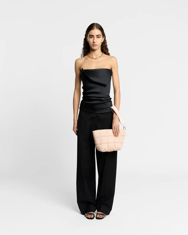 On-body picture of a woman carrying the Porter Clutch Bag in Cameo Rose by Vee Collective, wearing a minimalistic outfit against a clean studio background, with the attachable wristlet worn on her wrist.