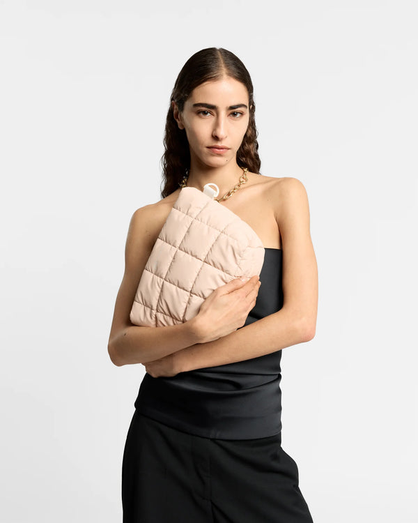 On-body picture of a woman holding the Porter Clutch Bag in Barely Beige by Vee Collective in front of her body, wearing a minimalistic outfit against a clean studio background.