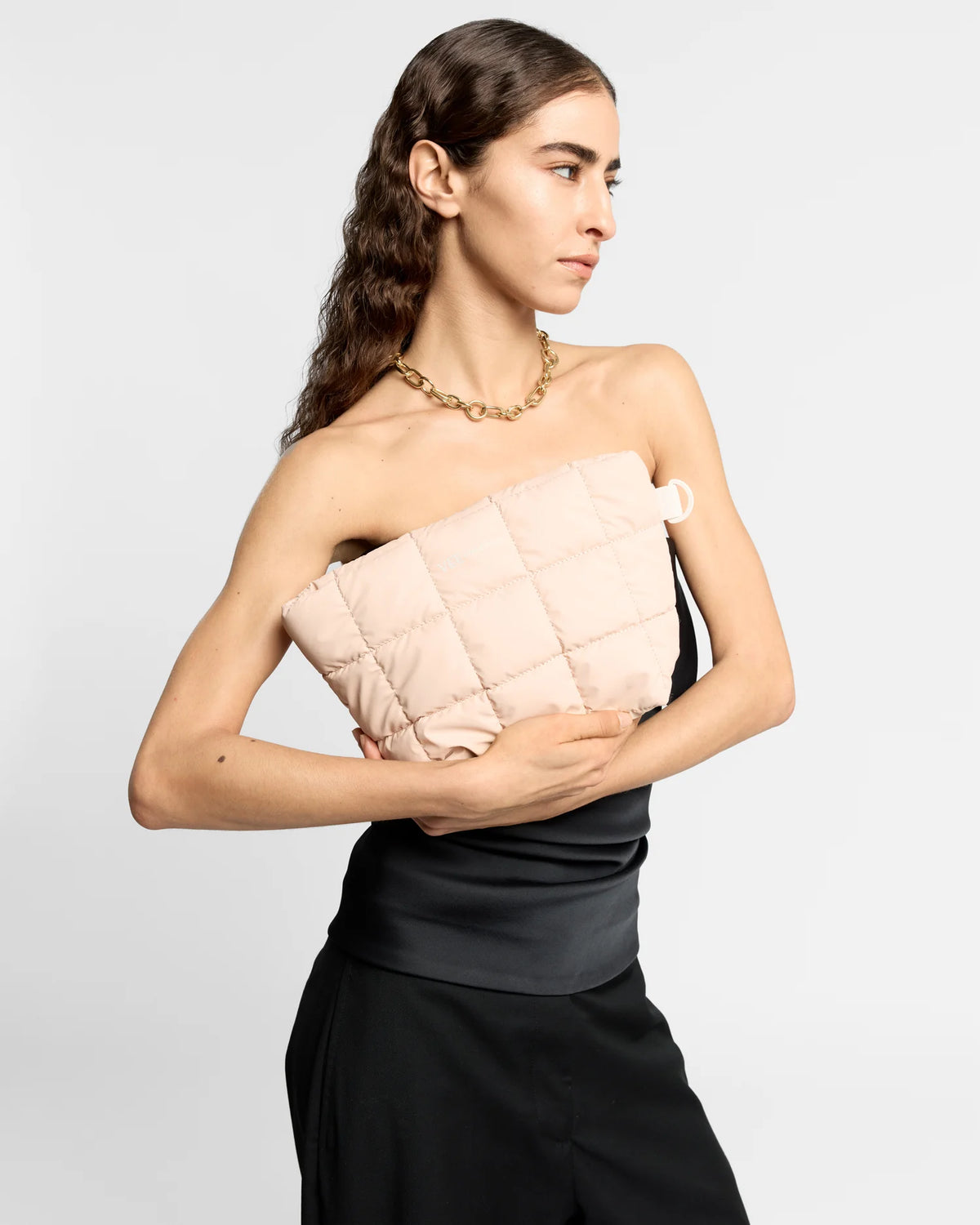 On-body picture of a woman holding the Porter Clutch Bag in Cameo Rose by Vee Collective in front of her body, wearing a minimalistic outfit against a clean studio background.