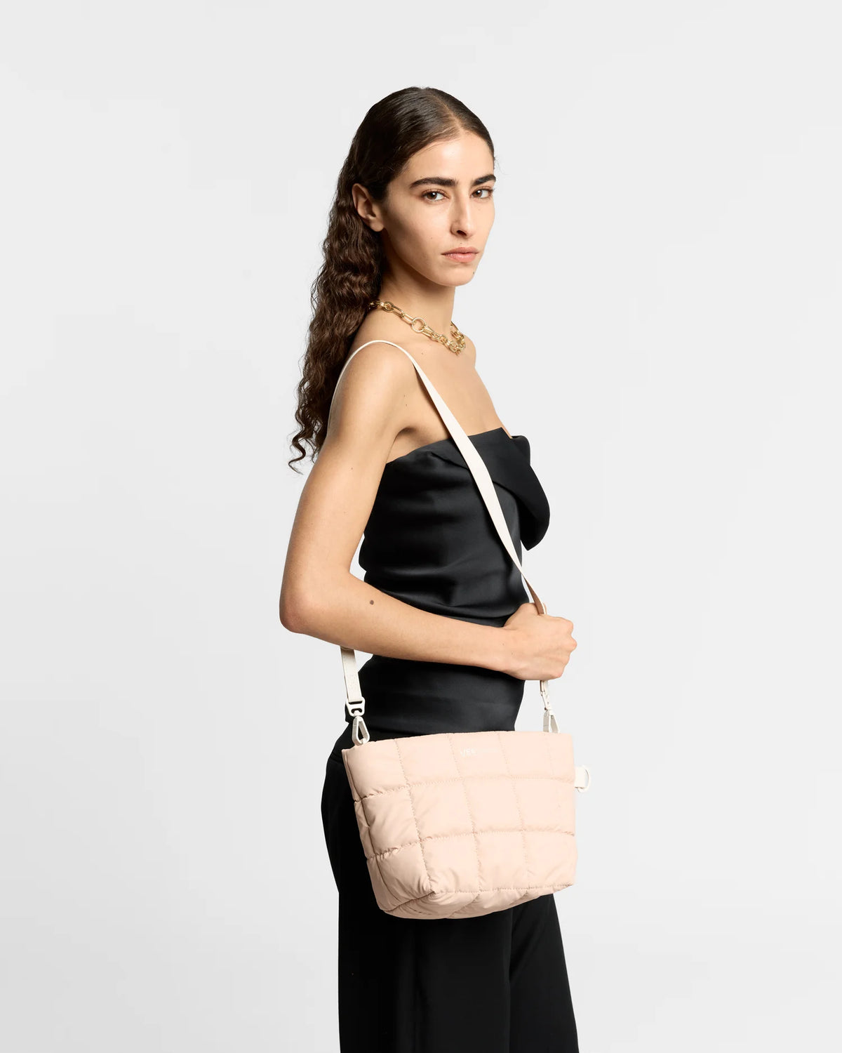On-body picture of a woman carrying the Porter Clutch Bag in Cameo Rose by Vee Collective over her shoulder with the attachable crossbody strap, wearing a minimalistic outfit against a clean studio background.