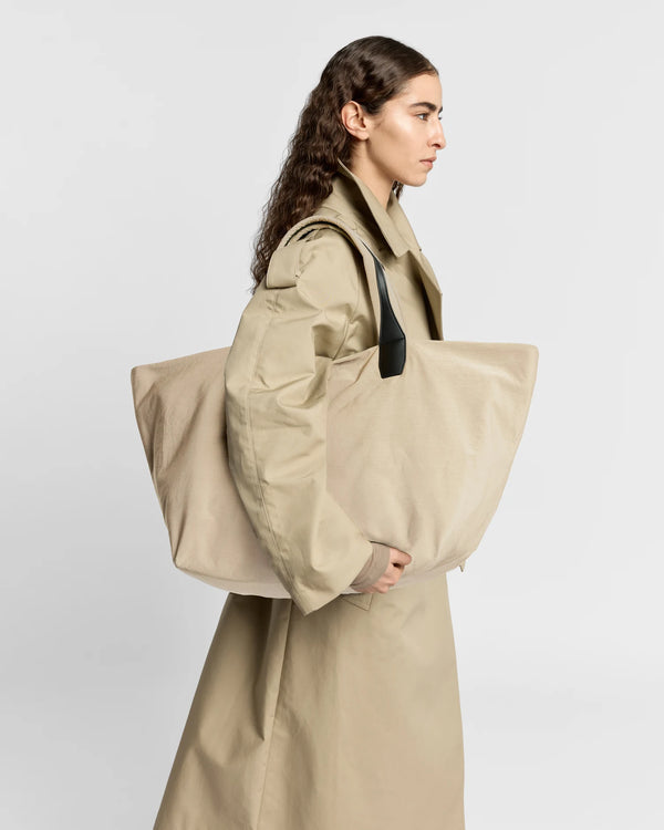 Woman in a beige trench coat carrying the Porter Essence Weekender Tote Bag in Beige Trench by Vee Collective against a plain studio background.