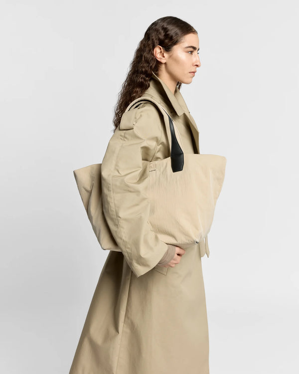 Woman in a beige trench coat carrying the Porter Essence Medium Tote Bag in Beige Trench by Vee Collective against a plain studio background.