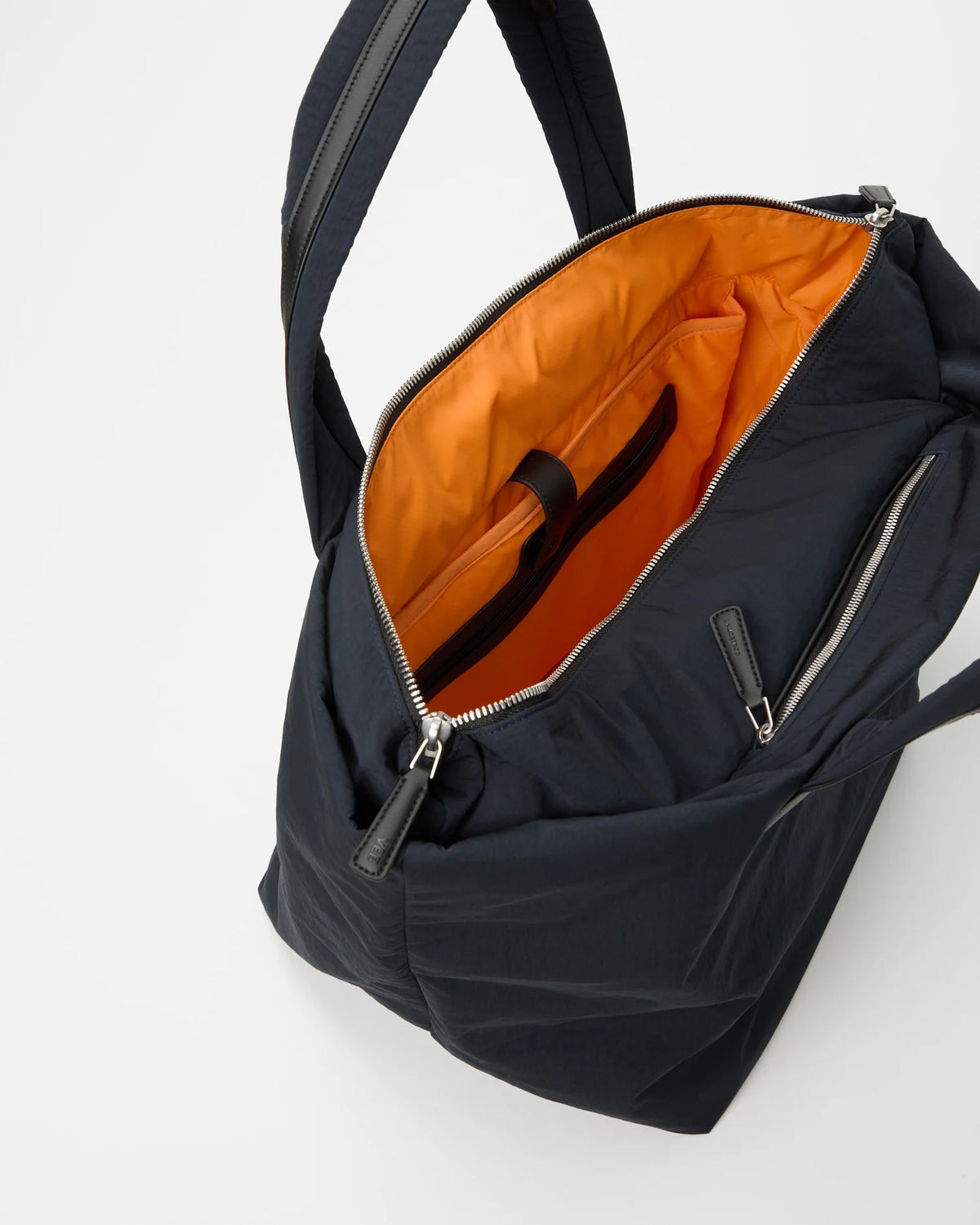 Open Vee Collective Porter Essence Medium in Midnight Trench, showing the quilted exterior, top zipper, and orange interior of the Tote bag.
