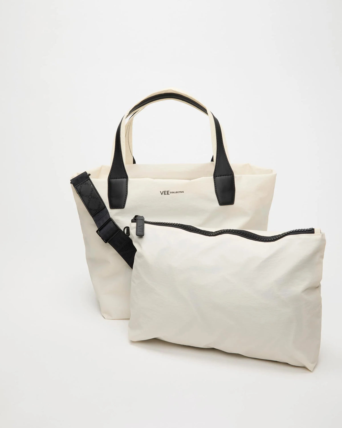 Front product image of the Vee Collective Porter Tote Essence Medium in off-white, shown with part of the removable crossbody strap visible and the matching pouch placed in front of the tote bag.