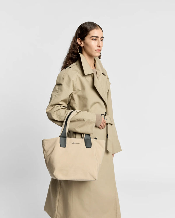 Woman in a beige trench coat carrying the Porter Essence Small Tote Bag in Beige Trench by Vee Collective against a plain studio background.