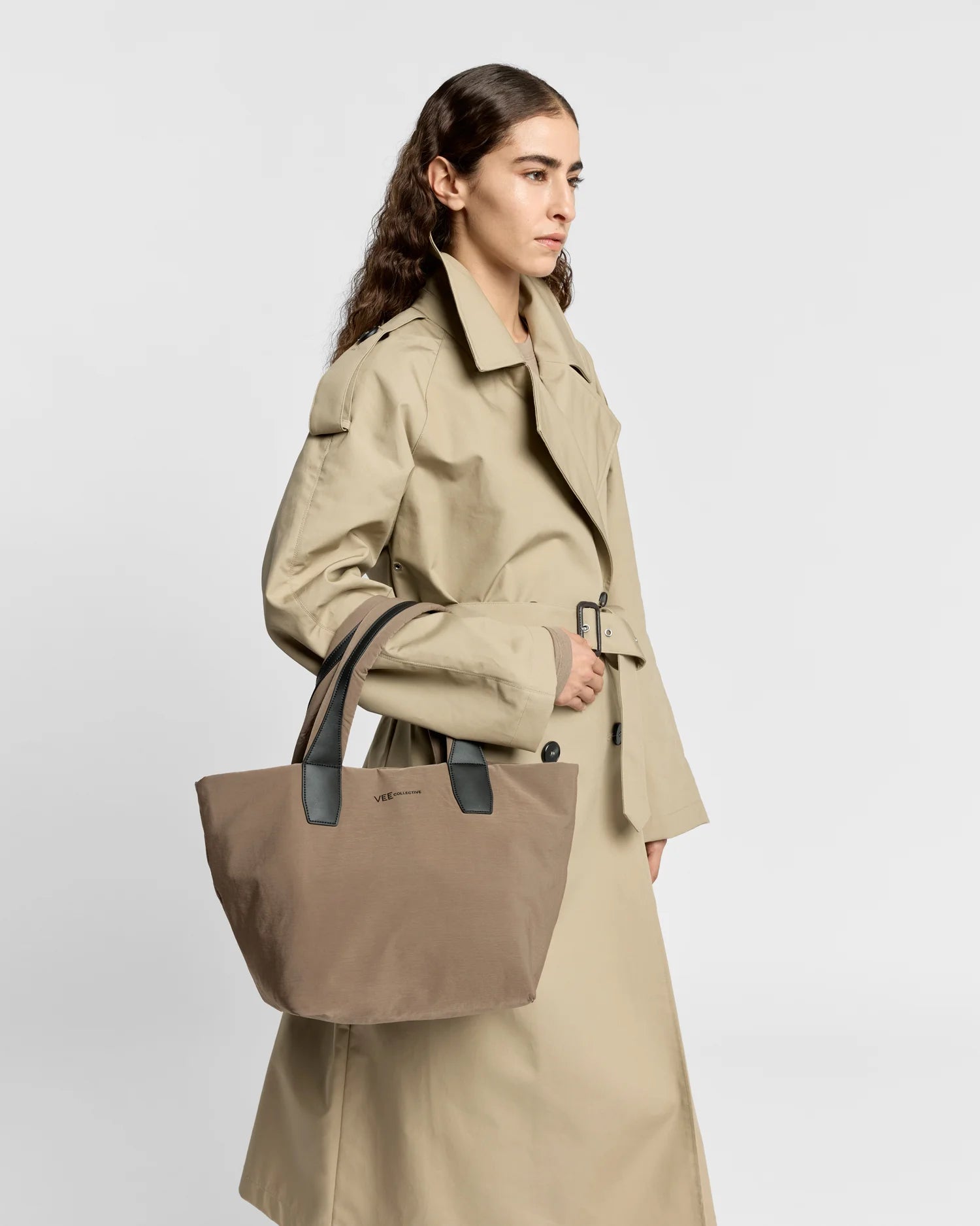 Woman in a beige trench coat carrying the Porter Essence Small Tote Bag in Mink Trench by Vee Collective against a plain studio background.