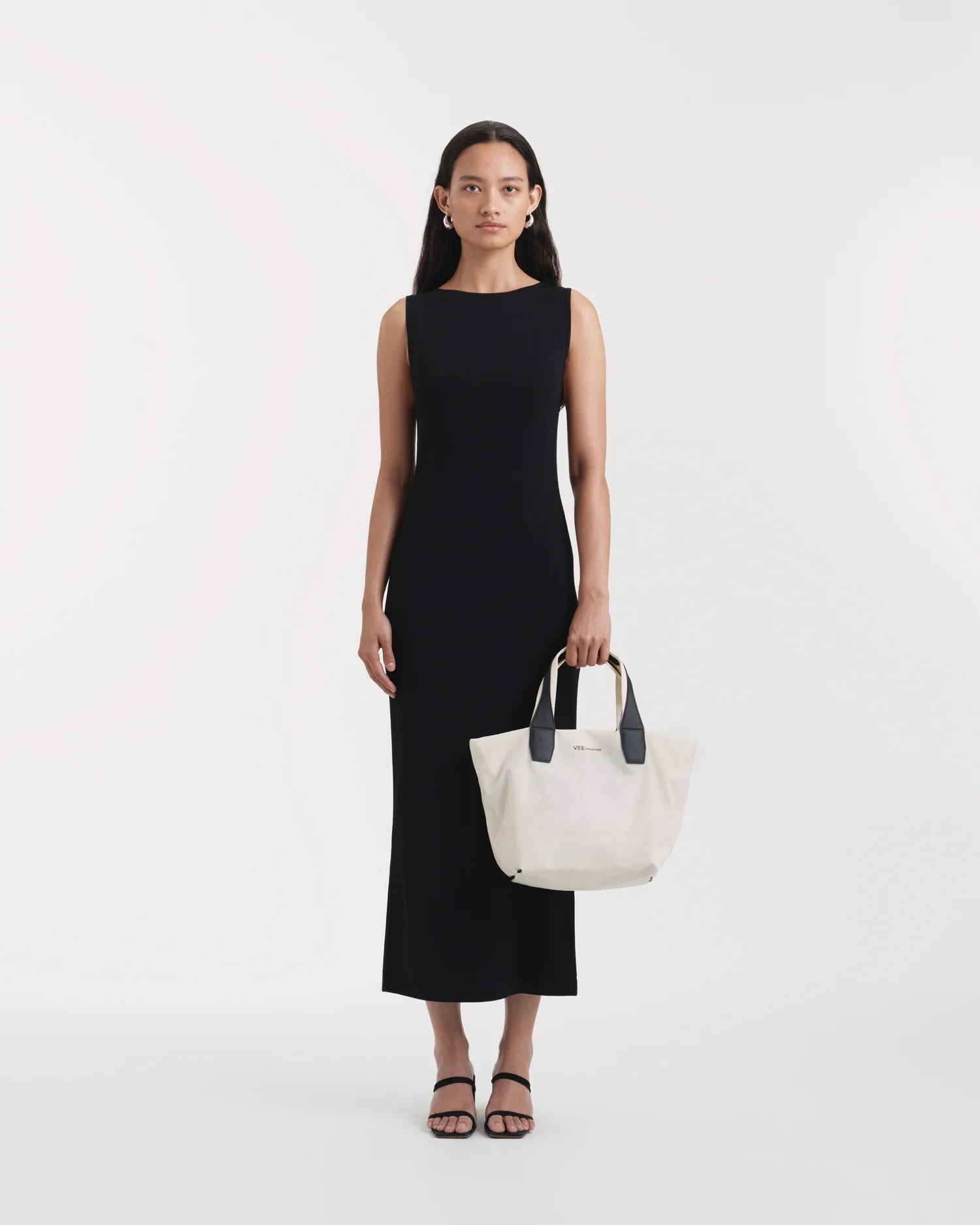 On-body view of a woman holding the Vee Collective Porter Tote Essence Small in off-white with an outstretched arm in front of her torso, showcasing the tote bag’s clean and minimal silhouette.