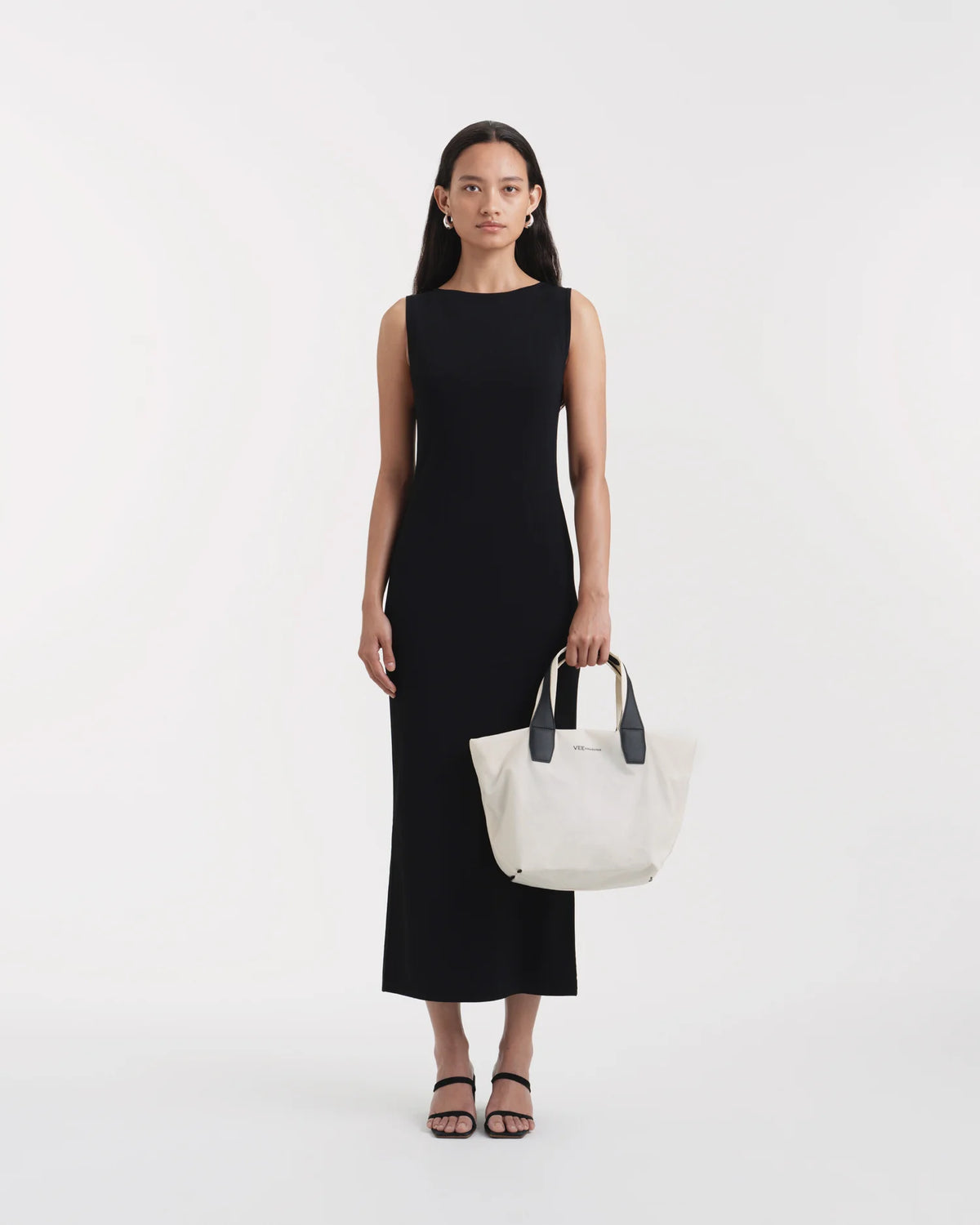 On-body view of a woman holding the Vee Collective Porter Tote Essence Small in off-white with an outstretched arm in front of her torso, showcasing the tote bag’s clean and minimal silhouette.