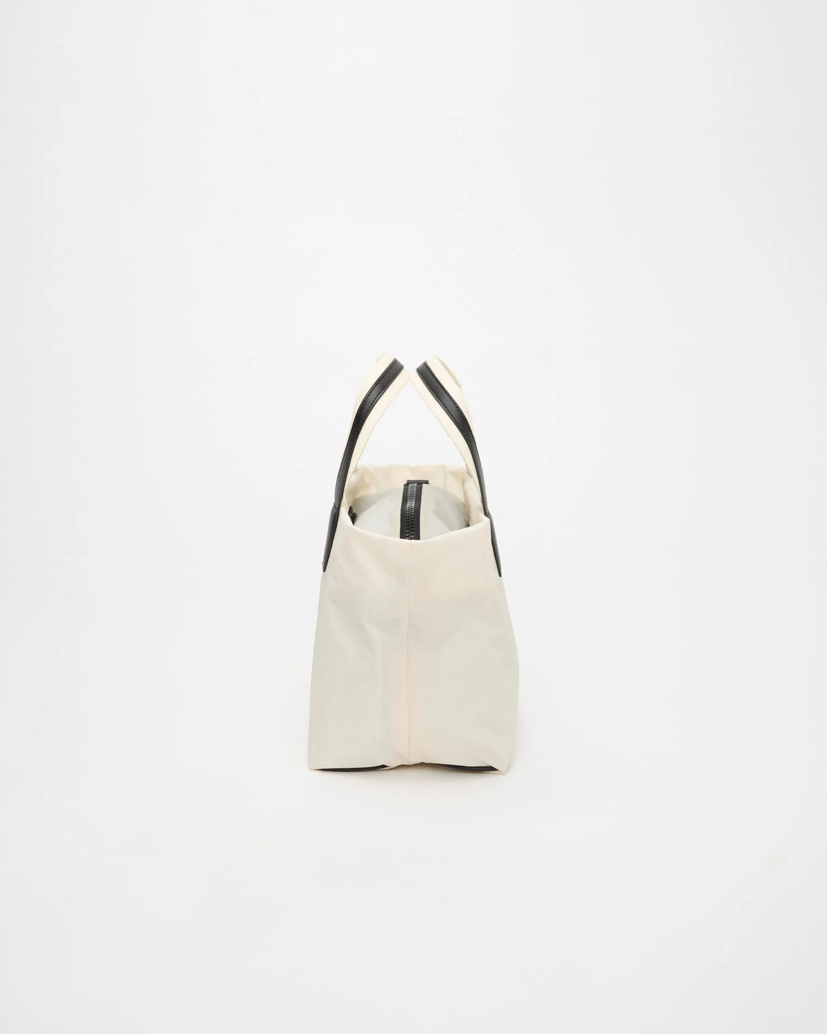 Side view product image of the Vee Collective Porter Essence Small Bag in off-white, highlighting the tote bag’s shape and minimalist detailing.