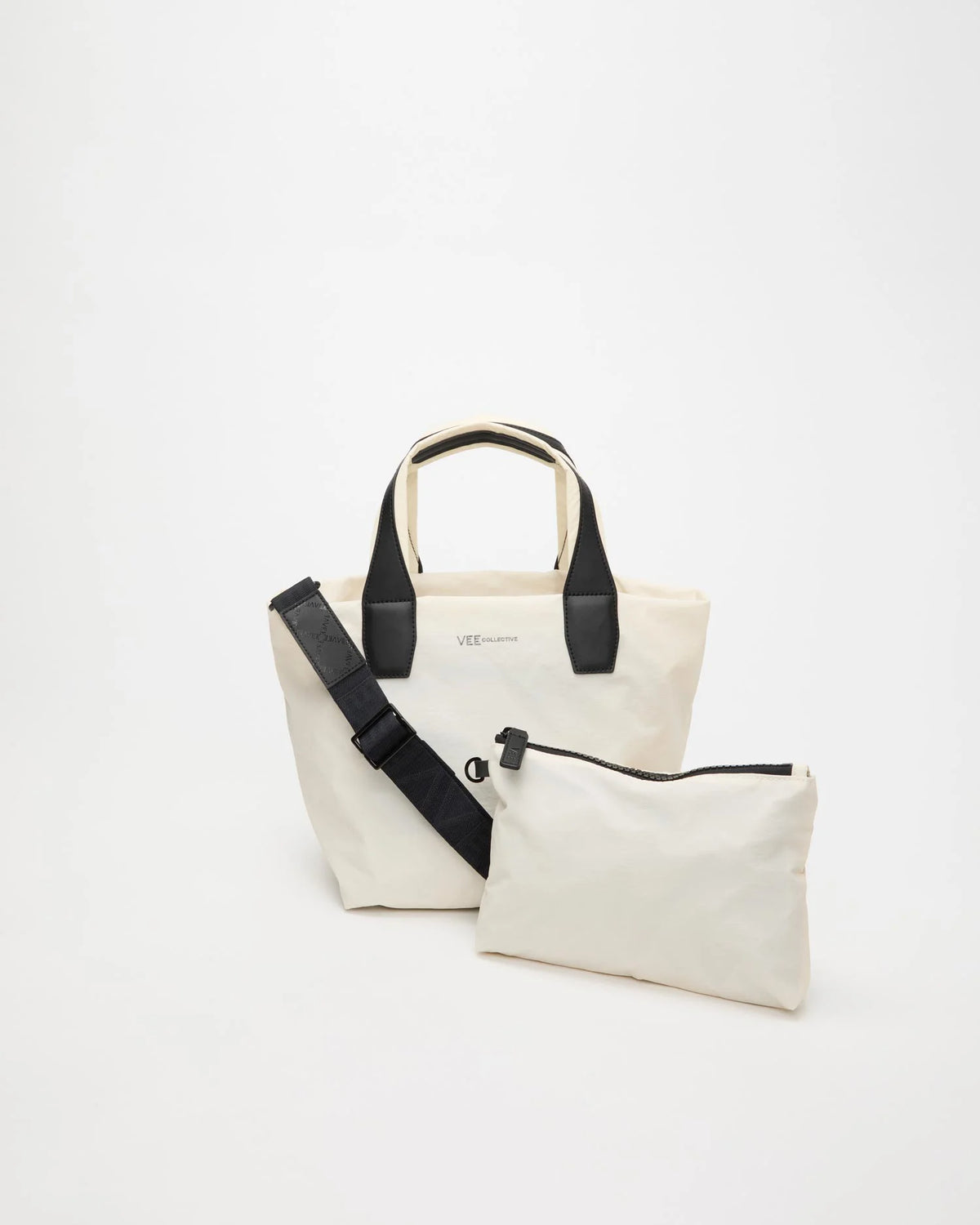 Front product image of the Vee Collective Porter Tote Essence Small in off-white, shown with part of the removable crossbody strap visible and the matching pouch placed in front of the tote bag.