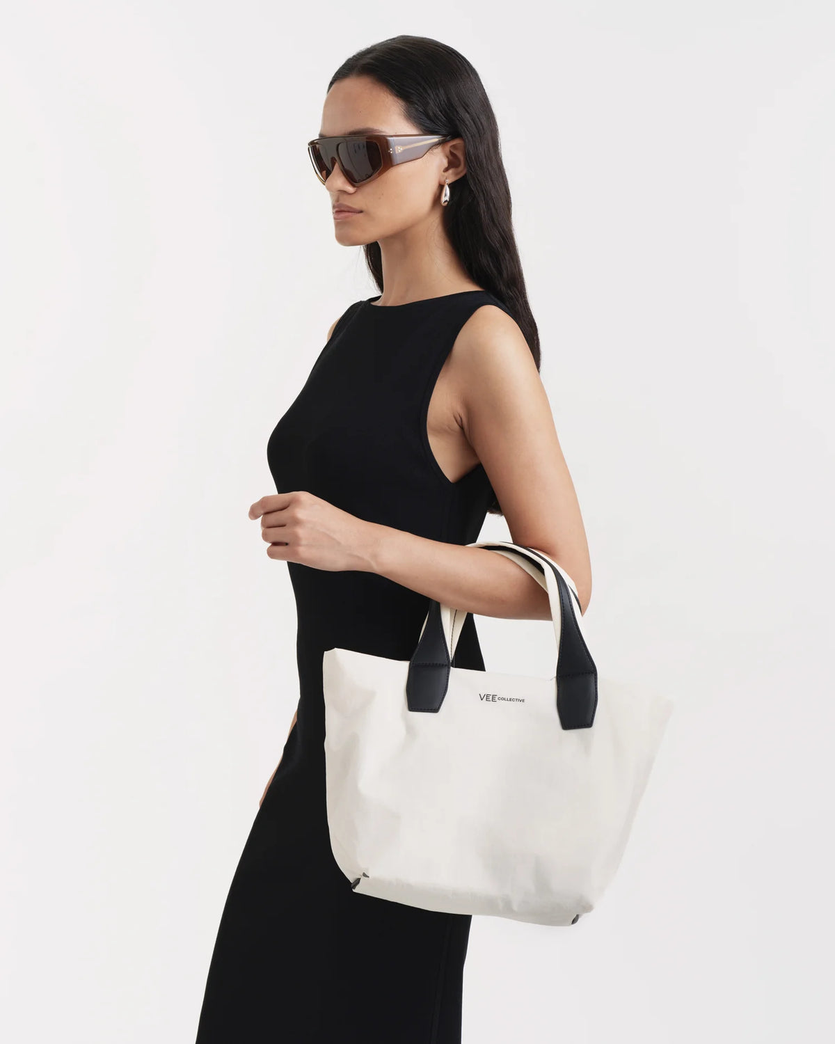Side view of a woman carrying the Vee Collective Porter Essence Small Tote Bag in off-white on her lower arm.