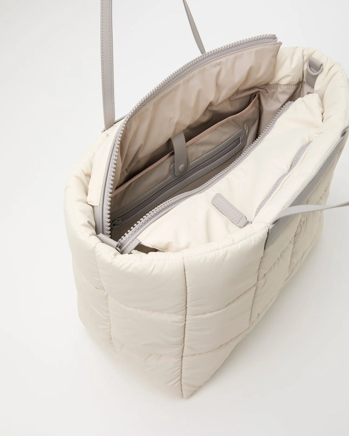 Open Vee Collective Porter Marché Large Tote Bag in Barely Beige, showing the quilted exterior, top zipper, and interior compartments of the tote bag.
