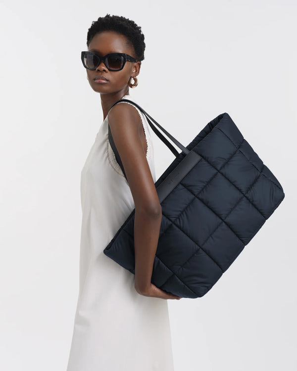 On-body picture of a woman carrying the Porter Marché Large Tote Bag in Dark Navy by Vee Collective, wearing a minimalistic outfit against a clean studio background.
