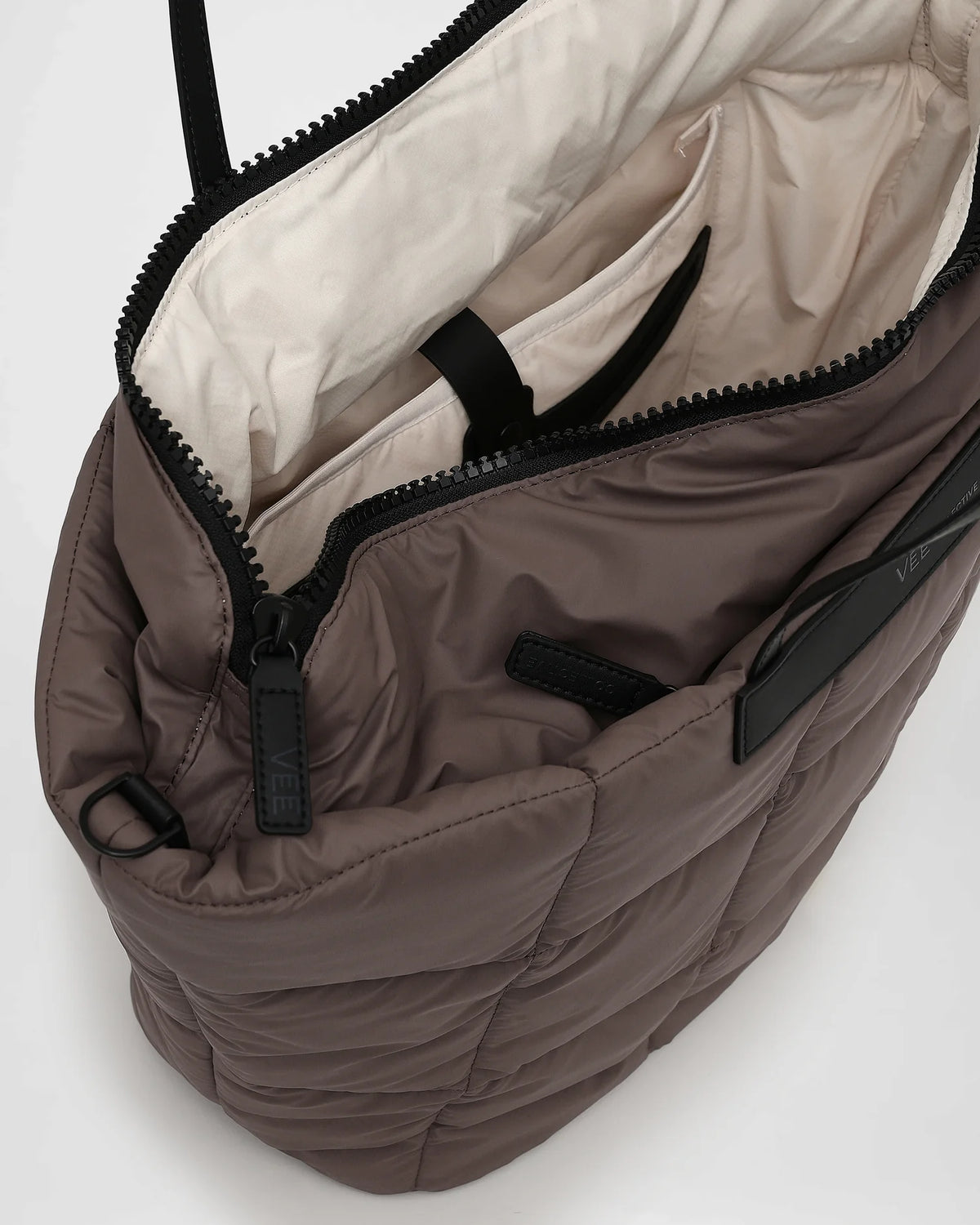 A close-up photo of an open Porter Tote in mink bag featuring black zippers and a light beige interior lining, set against a white background.