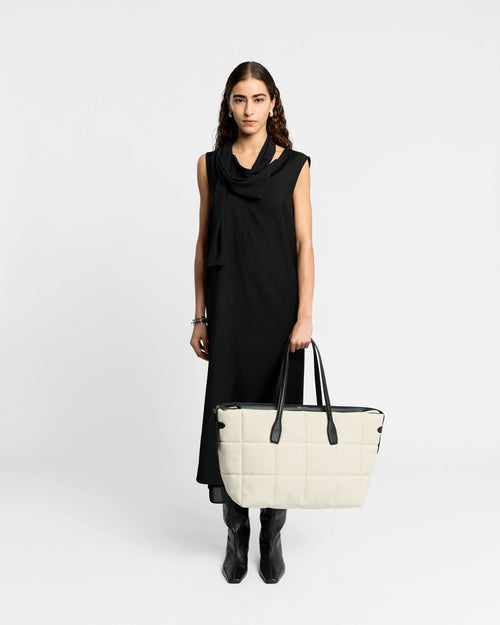 Large Tela Tote in natural canvas with black leather trim carried by a model in a black dress