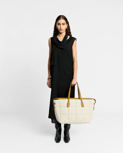 Model wearing a black dress holding a Tela Tote large natural tan canvas with tan leather handles