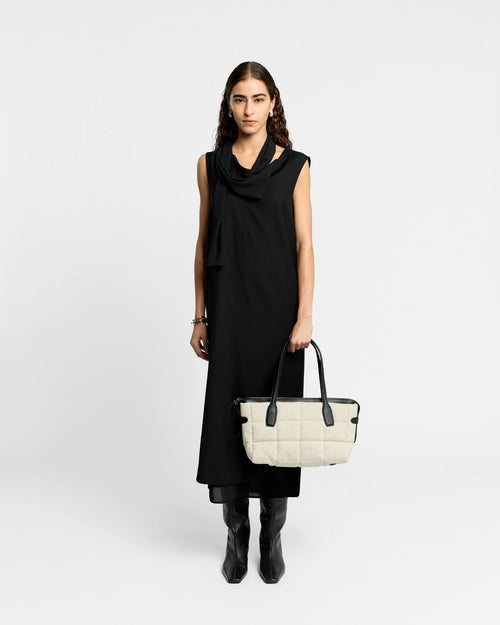 Model in a black dress holds a Tela Tote in natural canvas with black leather handles.