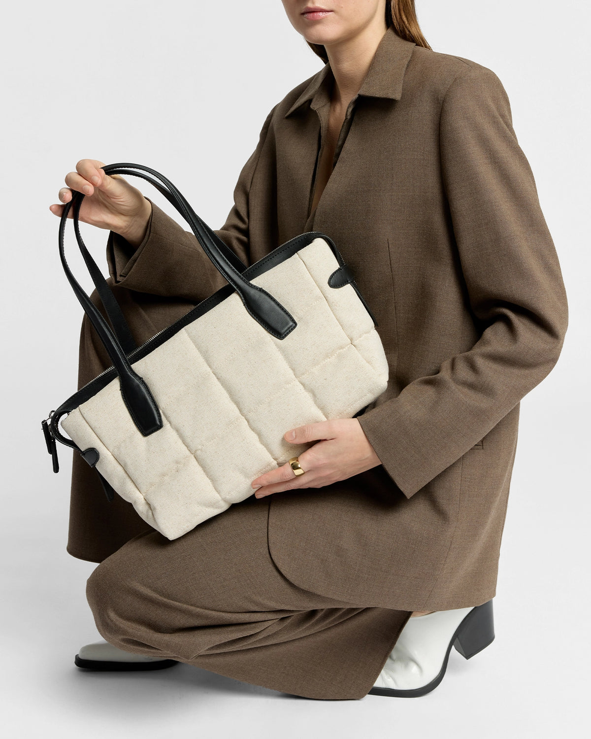 Beige Tela Tote with black leather handles held by a person in a brown suit