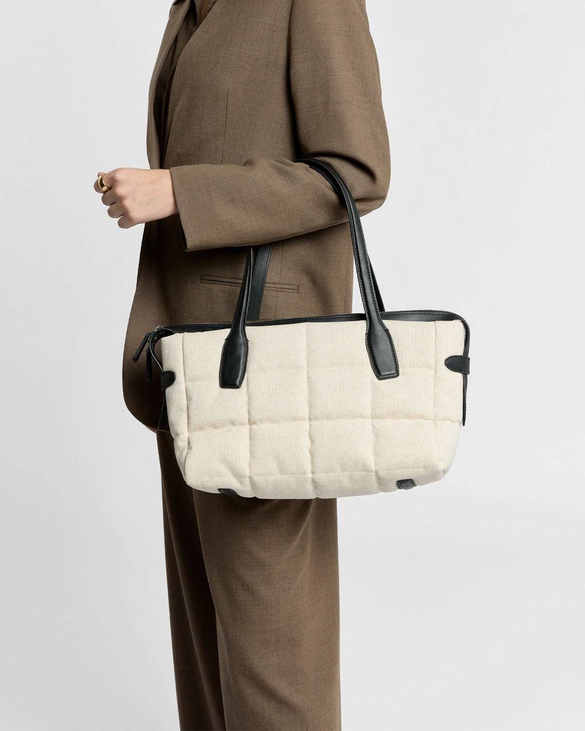 Woman in a brown suit carries a Tela Tote with natural canvas body and black leather handles.