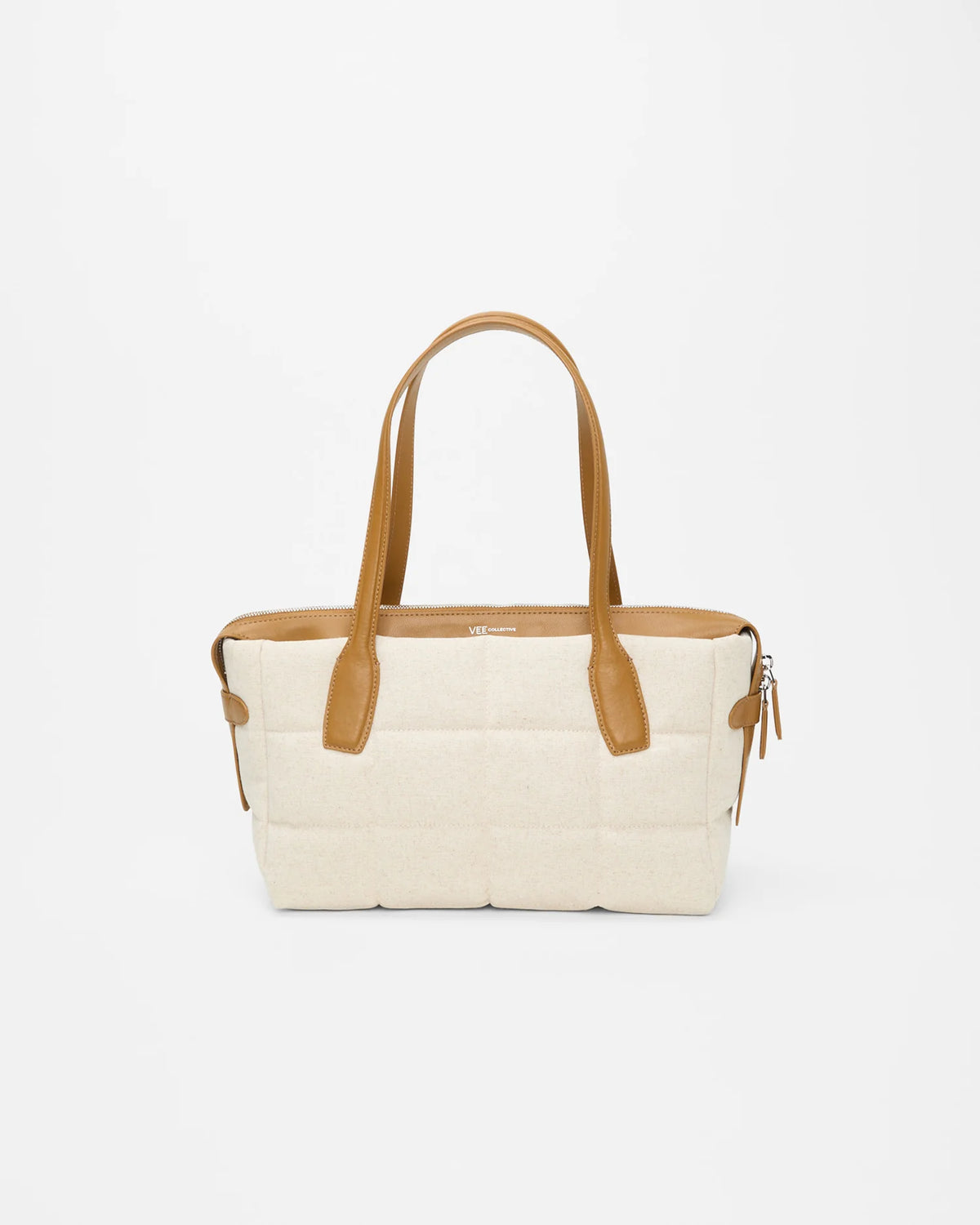 Model wearing a black dress holds Tela Tote Small Natural Tan Canvas with tan leather handles.