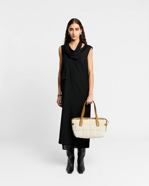 Model in black dress carries Tela Tote Small Natural Tan Canvas with tan leather handles.