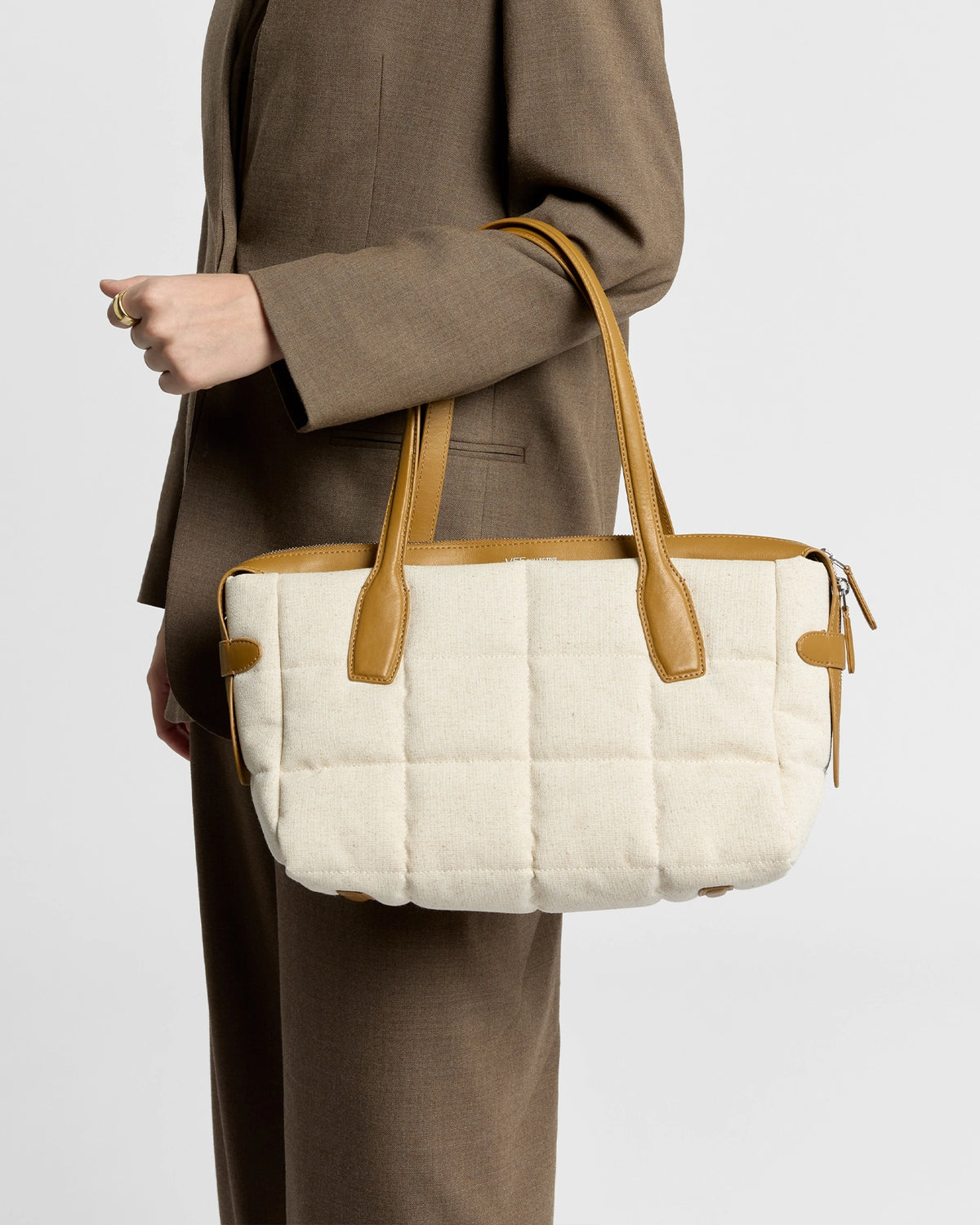 Model holding Tela Tote in natural canvas with tan leather handles.