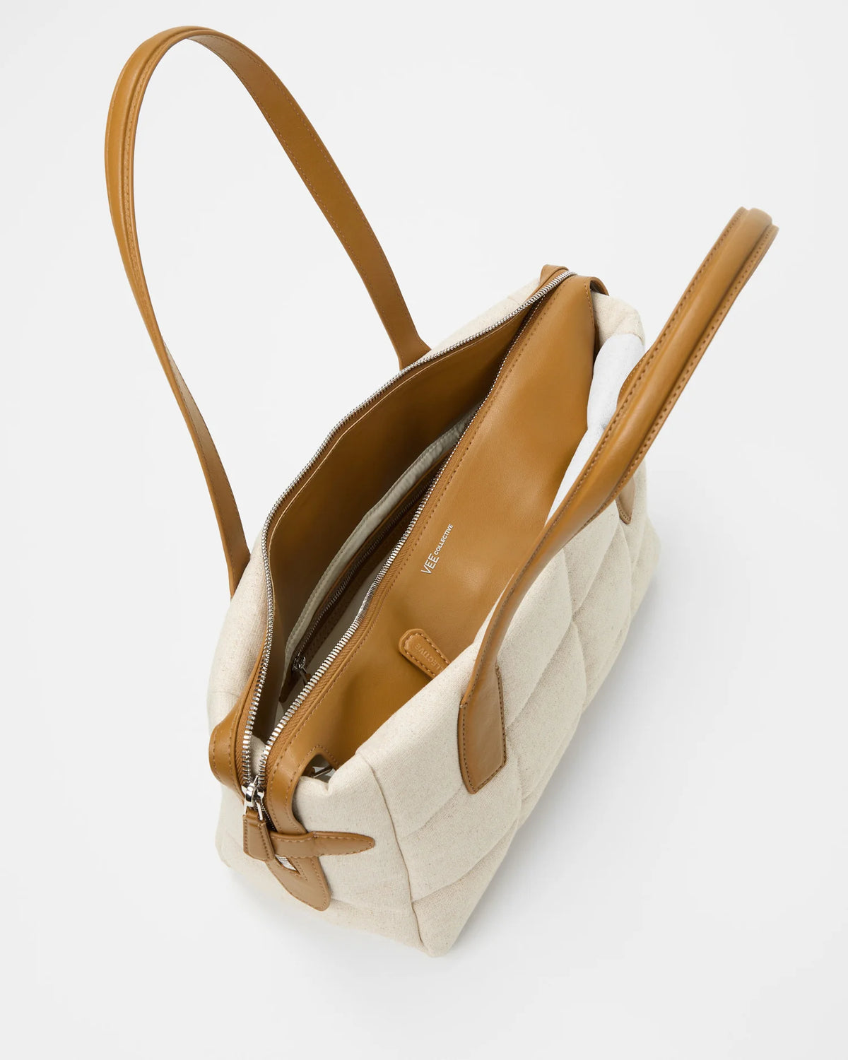 Top view of Tela Tote in natural canvas with tan leather trim and open zipper showing interior compartments.