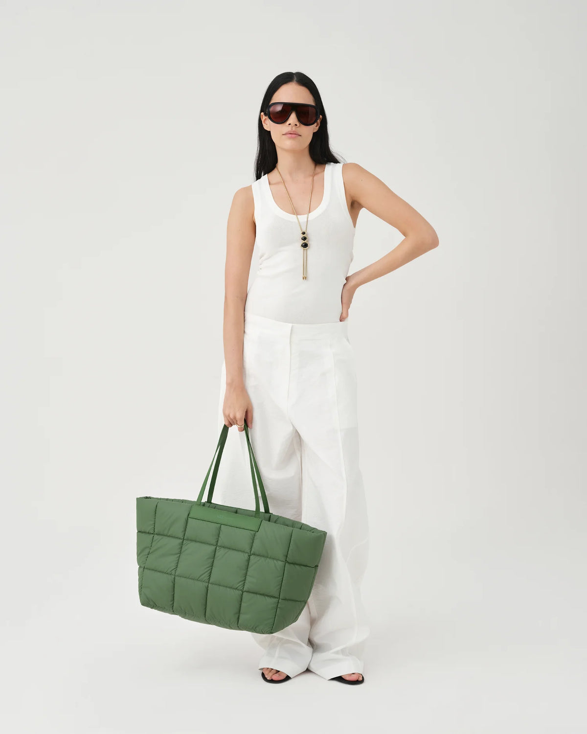 A photo of a woman wearing sunglasses and a white dress, carrying a large apple green Porter Tote Bag with a gold-tone zipper and strap hardware against a plain white studio background.