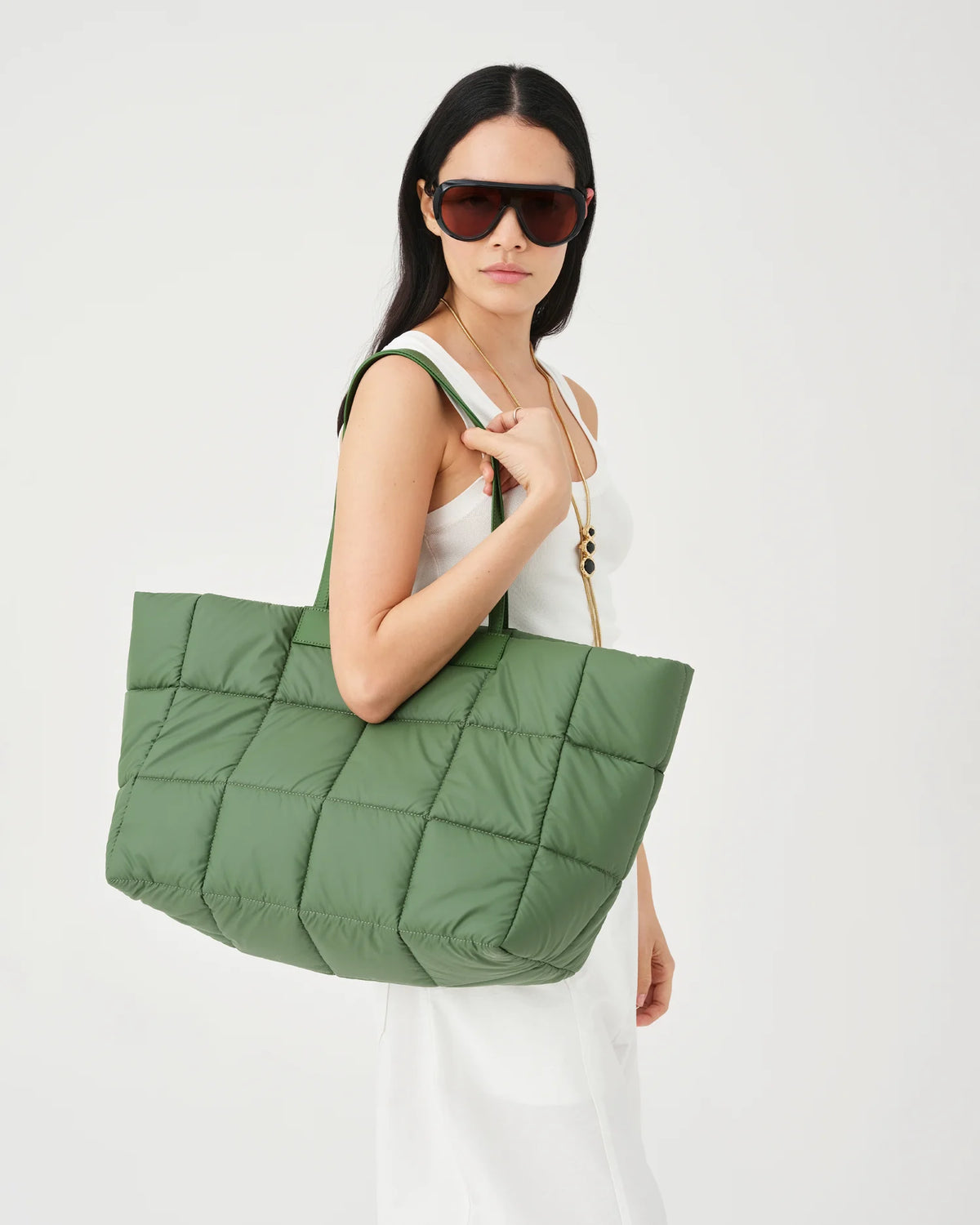 A photo of a woman wearing sunglasses and a white dress, carrying a large apple green Porter Tote Bag with a gold-tone zipper and strap hardware against a plain white studio background.
