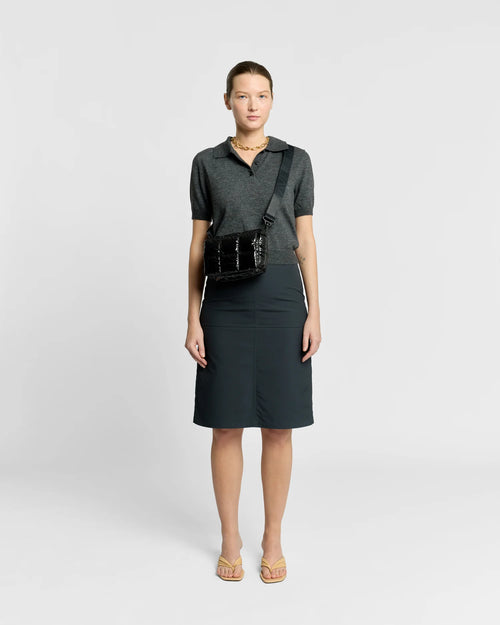 Woman in a minimal, clean outfit carrying the Vee Collective Porter Messenger Mini Bag in Black Vinyl, shown with its crossbody strap.