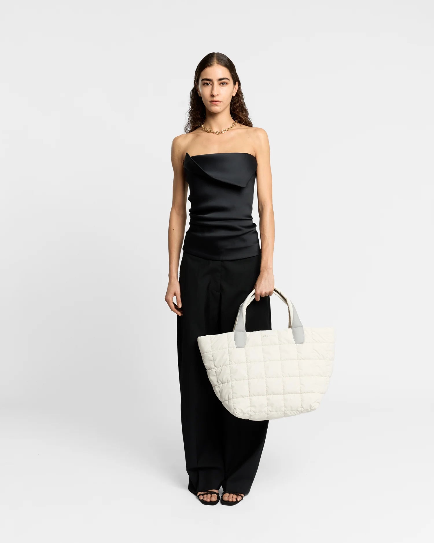 On-body picture of a woman holding the Medium Porter Tote Bag in Barely Beige by Vee Collective, wearing a minimalistic outfit against a clean studio background.